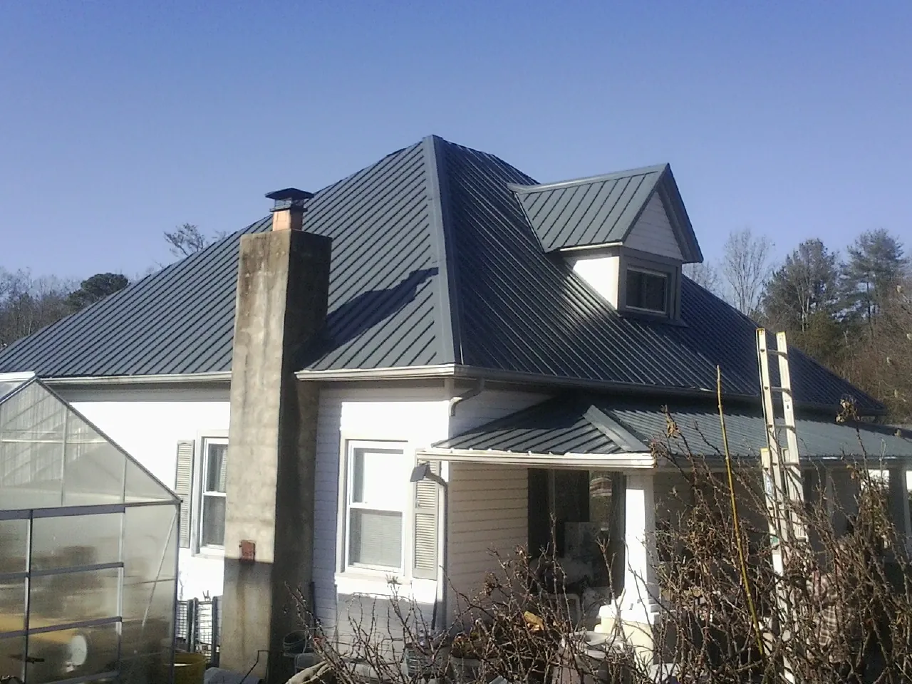 Dark blue standing seam metal roof on a white farmhouse with dormer — Slate & Tile Roof Repair by Roofing Brothers in Richfield